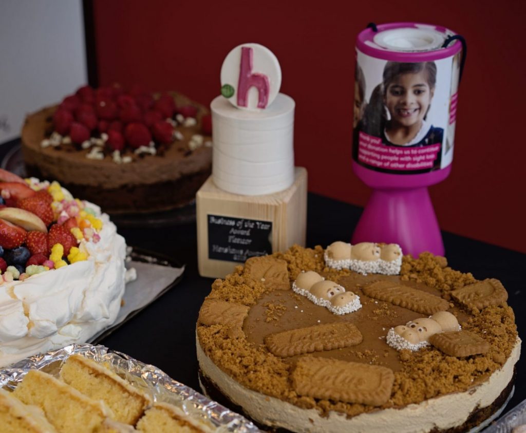 A selection of cakes on a table next to a Henshaws award and pink collection tin