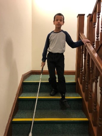 Boy walking down stairs with a white cane.