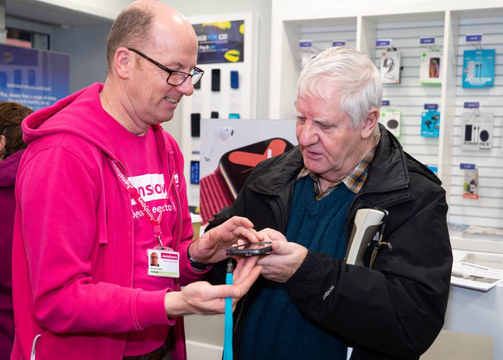 Image shows a member of Henshaws staff demonstrating a smartphone to a visually impaired man.