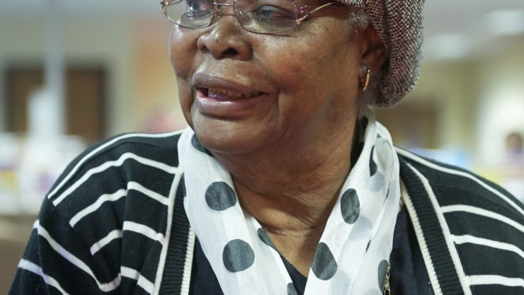 Image shows an elderly lady wearing glasses and smiling. She is wearing a spotty scarf.