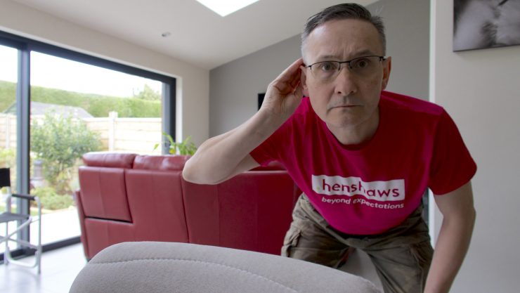 Image shows a man wearing a pink Henshaws t-shirt. He is cupping his hand to his ear.