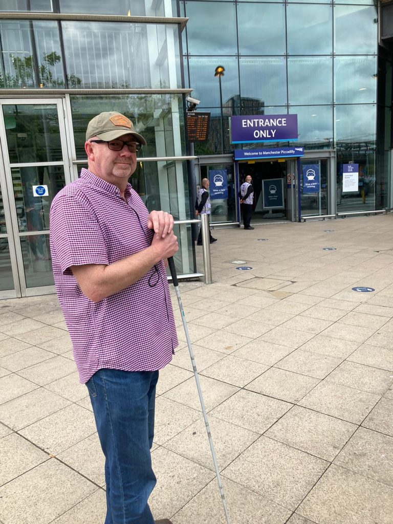 Simon holding long cane at Piccadilly station