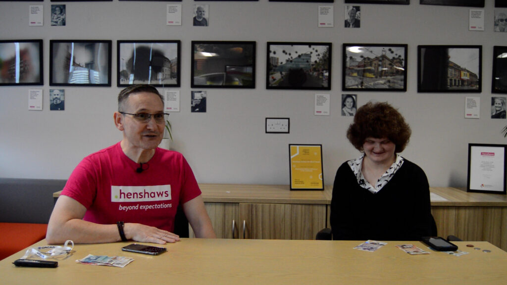 Mark and Alice facing the camera, with money visible on the table