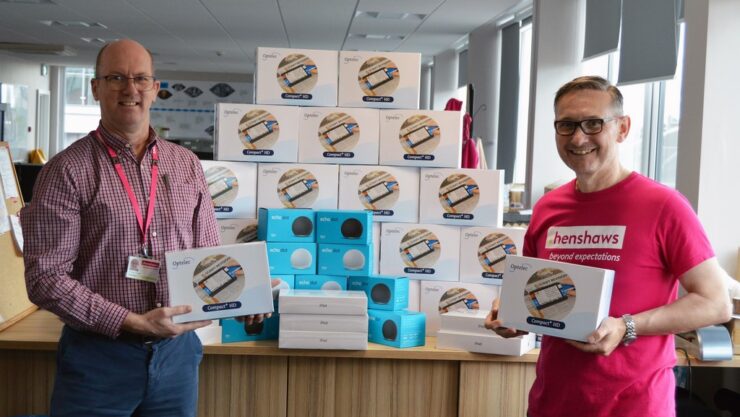 Two men with boxes of Optelec magnifiers, boxes of Amazon Echos and iPads