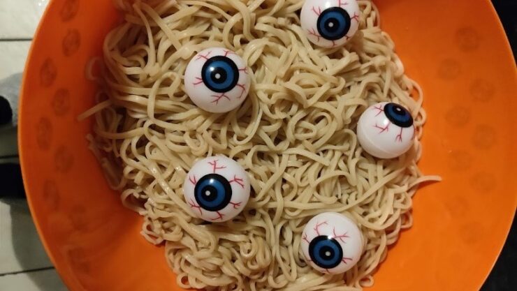 Noodles with spooky eyeballs in an orange bowl
