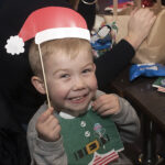 Child smiling to camera holding up a Santa hat to their head