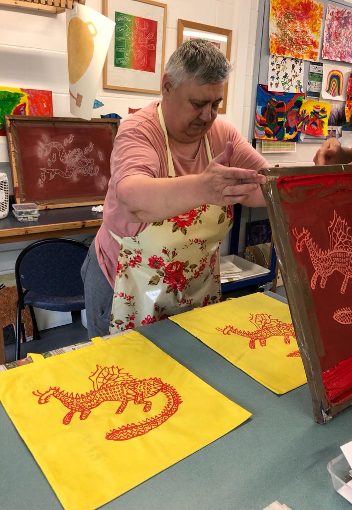 Anne is shown screen printing a red dragon onto yellow t shirts